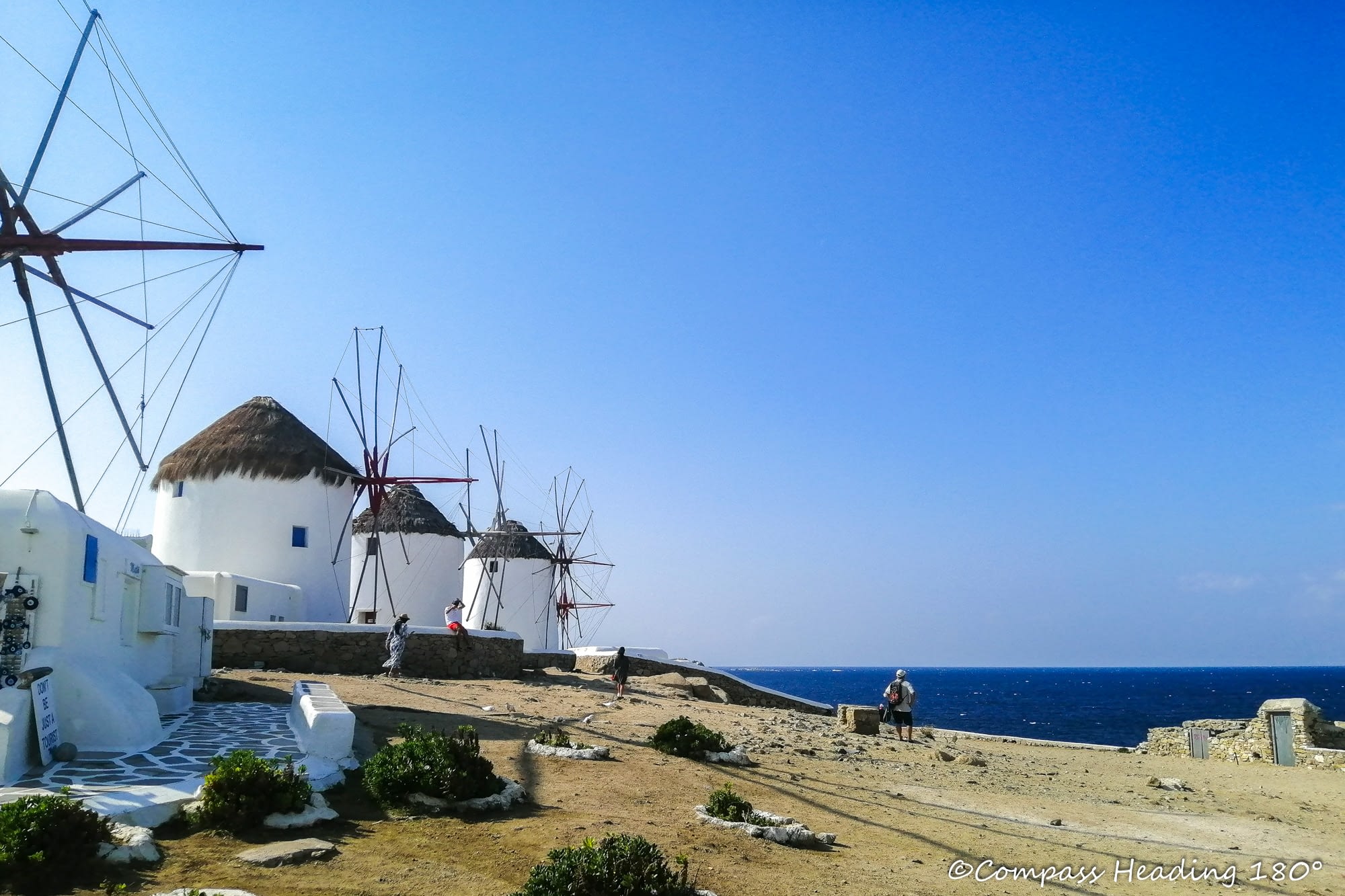 Mykonoksen kaupungin kuuluisat tuulimyllyt meren rannalla, taustalla sininen meri ja vaahtopäitä.