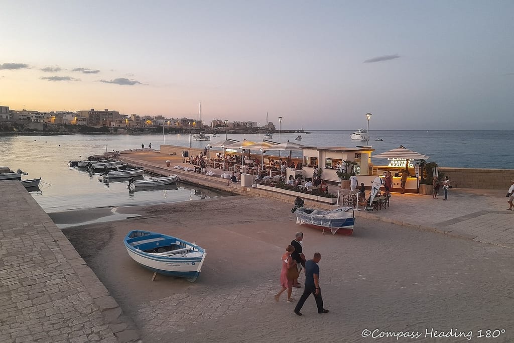 Otranto bay seen from town at twilight. A small beach, pier and beach bar in front, houses and hotels in the background.