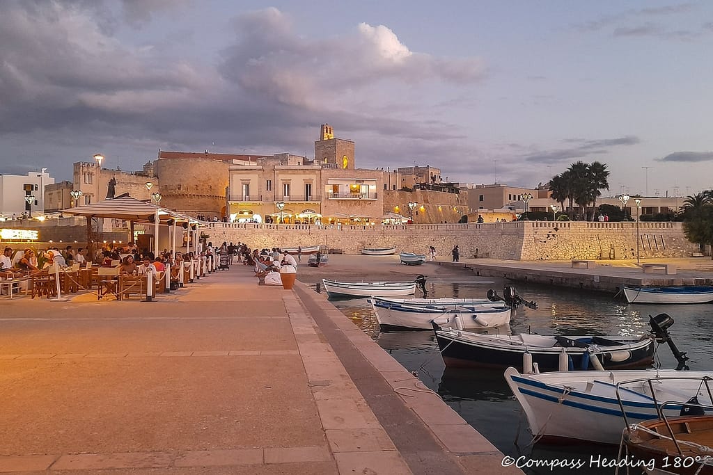 Small harbour in front of Otranto with wooden fishing boats. Walled town in the backyard with castle towers and church bell tower rising above.