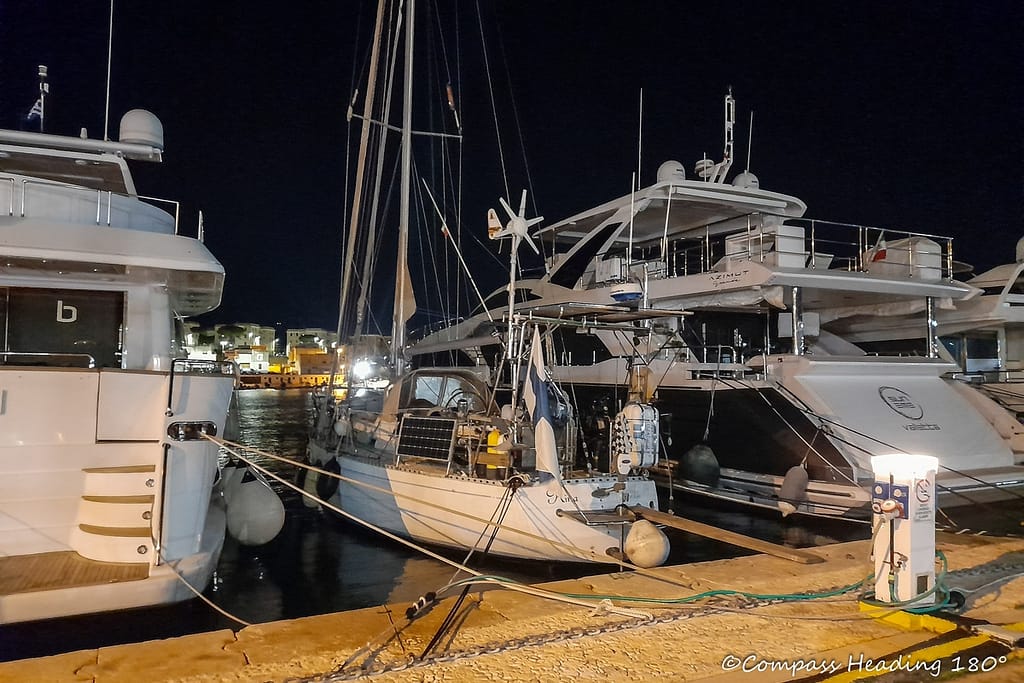 Night time picture of our white sailboat between two large motor yachts