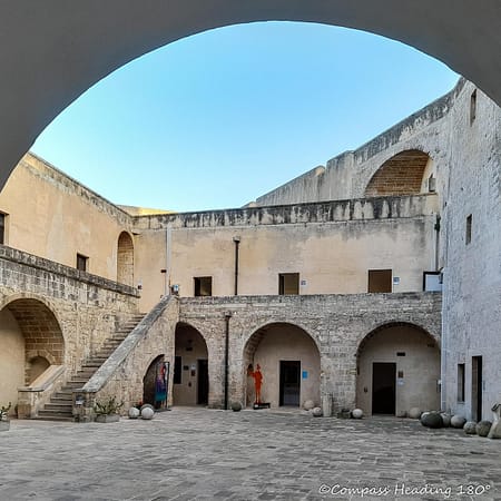 Castle courtyard with arched doors and staircases, old stone and iron cannon balls stashed in the corners.