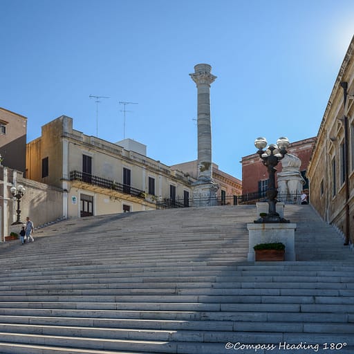 Massive stone staircase with old houses on both sides and a tall Roman column on the top platform