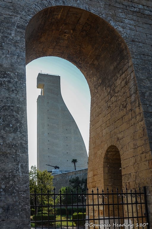 The large rudder shaped monument seen from the arch opening of a surrounding stone wall